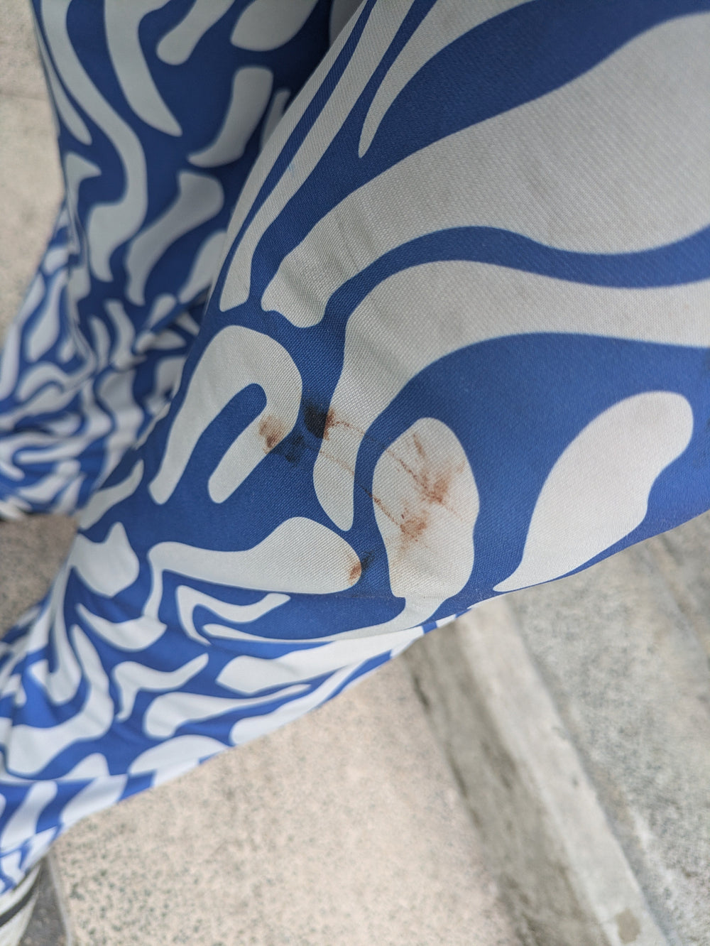 Blue and white patterned fabric with a small brown stain, shown close-up on a textured gray surface.