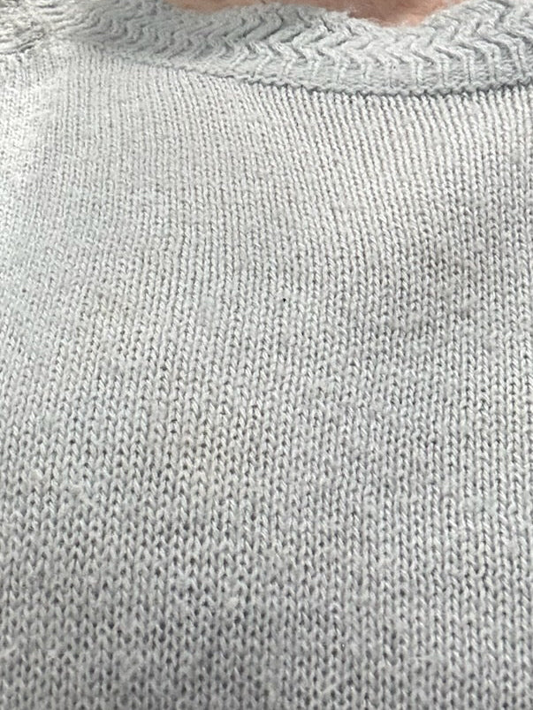 Close-up of a person wearing a light gray knit sweater, showing the neck, collar, and upper chest area.