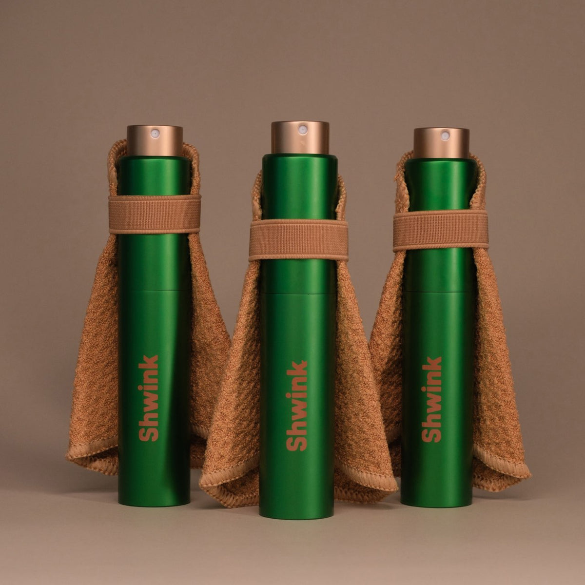 Three Shwink on-the-go stain spray bottles in matte with stain-lifting capes on a warm taupe background — travel stain remover spray.
