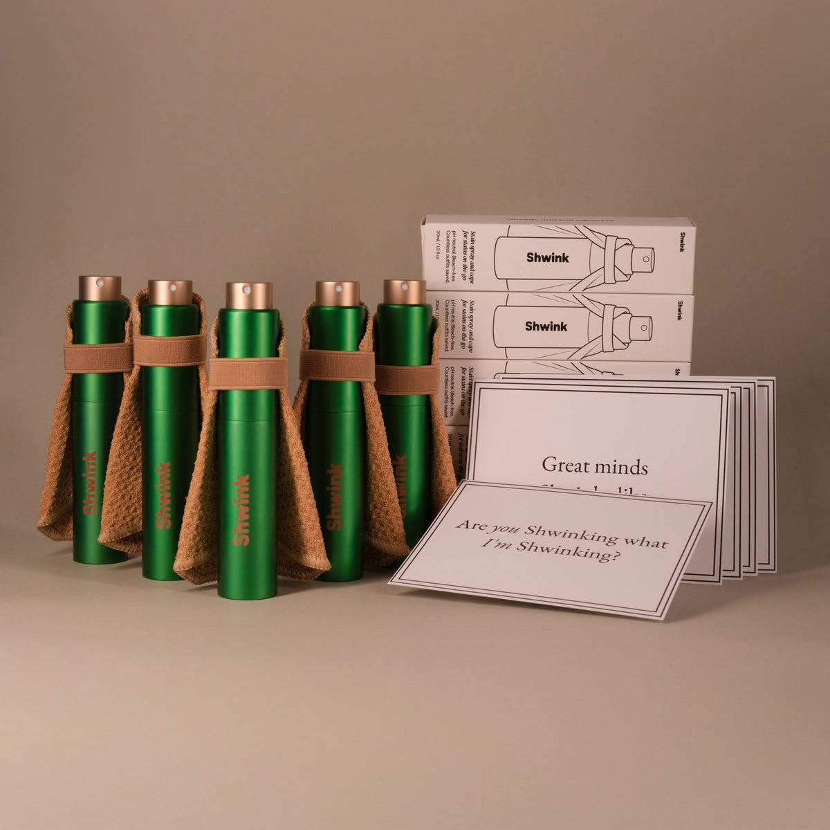 Five Shwink on-the-go stain sprays  and cape sets in matte finish with product boxes and gift cards on a warm taupe background — portable stain remover gift set.
