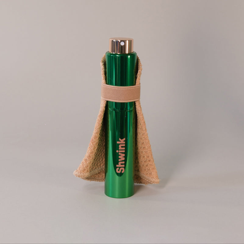 Shwink on-the-go stain spray (glossy green aluminium cylindrical tube with caramel stain lifting cape) twisted open. 