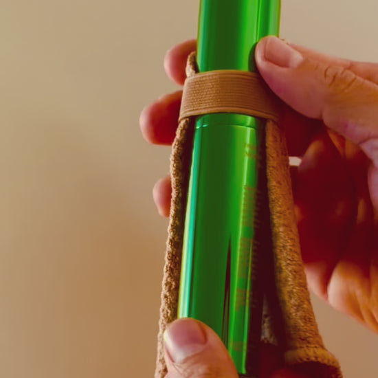 Shwink on-the-go stain spray (glossy green aluminium cylindrical tube with caramel stain lifting cape) being twisted open and two sprays. 