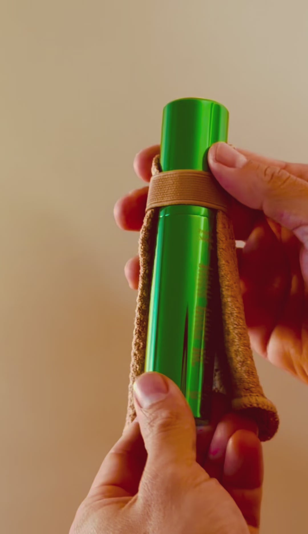 Shwink on-the-go stain spray (glossy green aluminium cylindrical tube with caramel stain lifting cape) being twisted open and two sprays. 