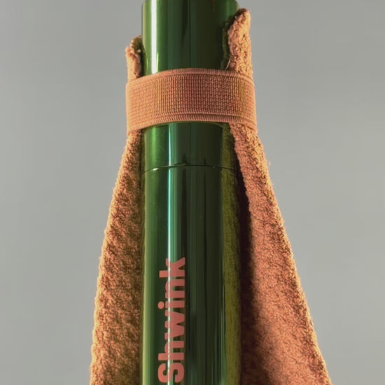 Shwink on-the-go stain spray (glossy green aluminium cylindrical tube with caramel stain lifting cape) slow motion video with lights. 